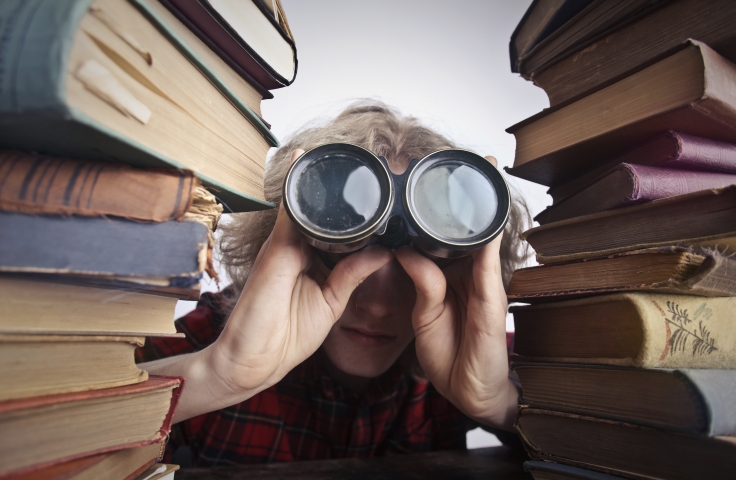 a boy holding a binocular looking through pile of books