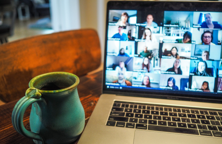 A laptop screen filled with a large Zoom chat and a coffee mug nearby. 
