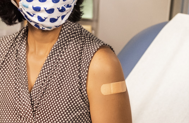 Woman wearing a mask with a Band-Aid on her left arm.