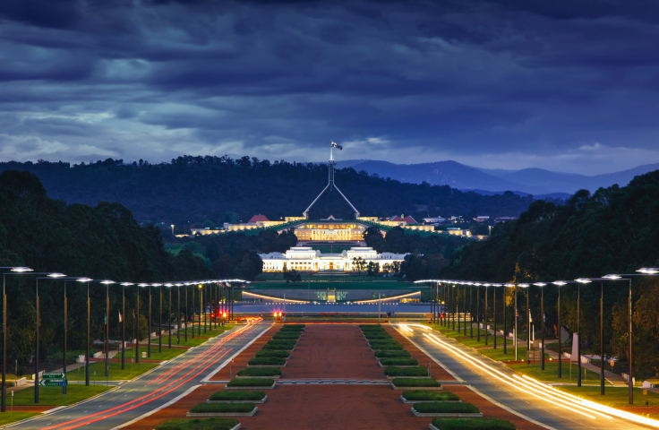 Parliament House (Australia) at dusk, shot from the perspective of the War Memorial. Lights line the avenue leading to Parliament House in the near distance.